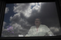 In this photo taken on Wednesday, April 29, 2020, Diane Wanten, 61, poses as she looks out of the window of the house of her son in Alken, Belgium. Wanten was recently released into home quarantine after being treated for two weeks at the Jessa Hospital ICU ward for COVID-19 coronavirus patients. (AP Photo/Francisco Seco)