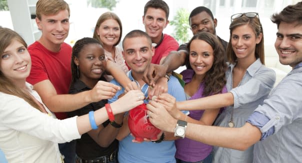 Group of young people inserting coins to a piggy bank.