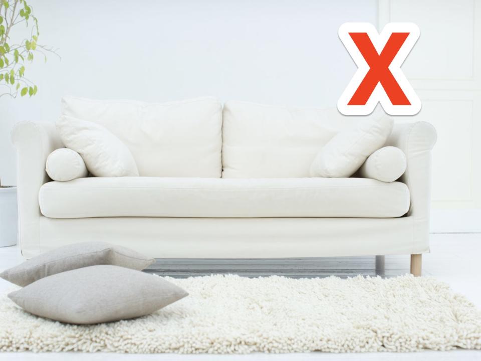 White couch, pillows, rug, floor, and walls with a red X in upper right corner