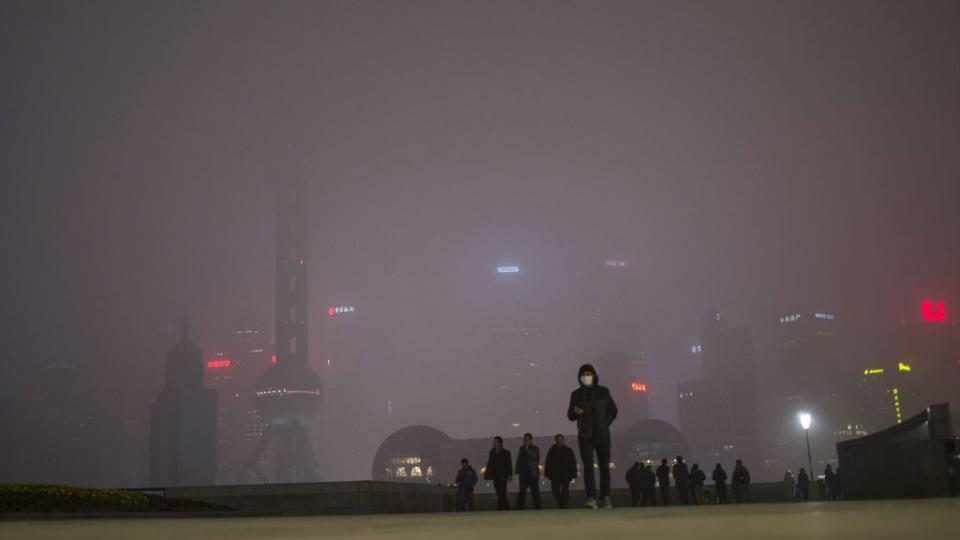 A man wearing an air mask walks through downtown Shanghai, China. The sky is filled with smog.