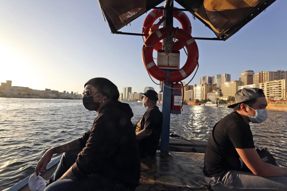 From left to right, Eric Roman, vocalist, Jeff Zacarias, AJ, president of the Dubai Filipino performers' union and Rommel Cuison, guitarist cross the creek water on a boat in Dubai, United Arab Emirates, Wednesday, Oct. 28, 2020. As the coronavirus pandemic mutes Dubai's live-music scene, the Filipino show bands that long have animated the city's storied nightlife are being disproportionately squeezed. Many are out of work and out of money, struggling to survive in overcrowded dormitories at the mercy of employers (AP Photo/Kamran Jebreili)