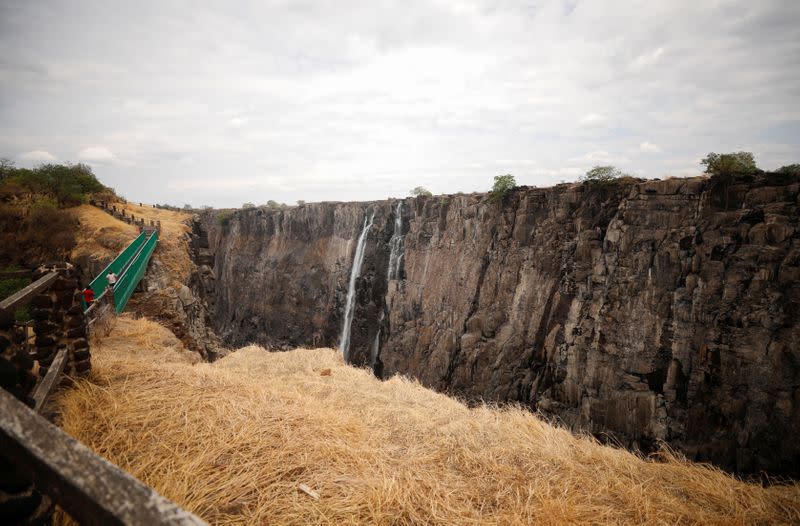 Visitors walk over a bridge as dry cliffs are seen along the parched gorge on the Zambian side of Victoria Falls