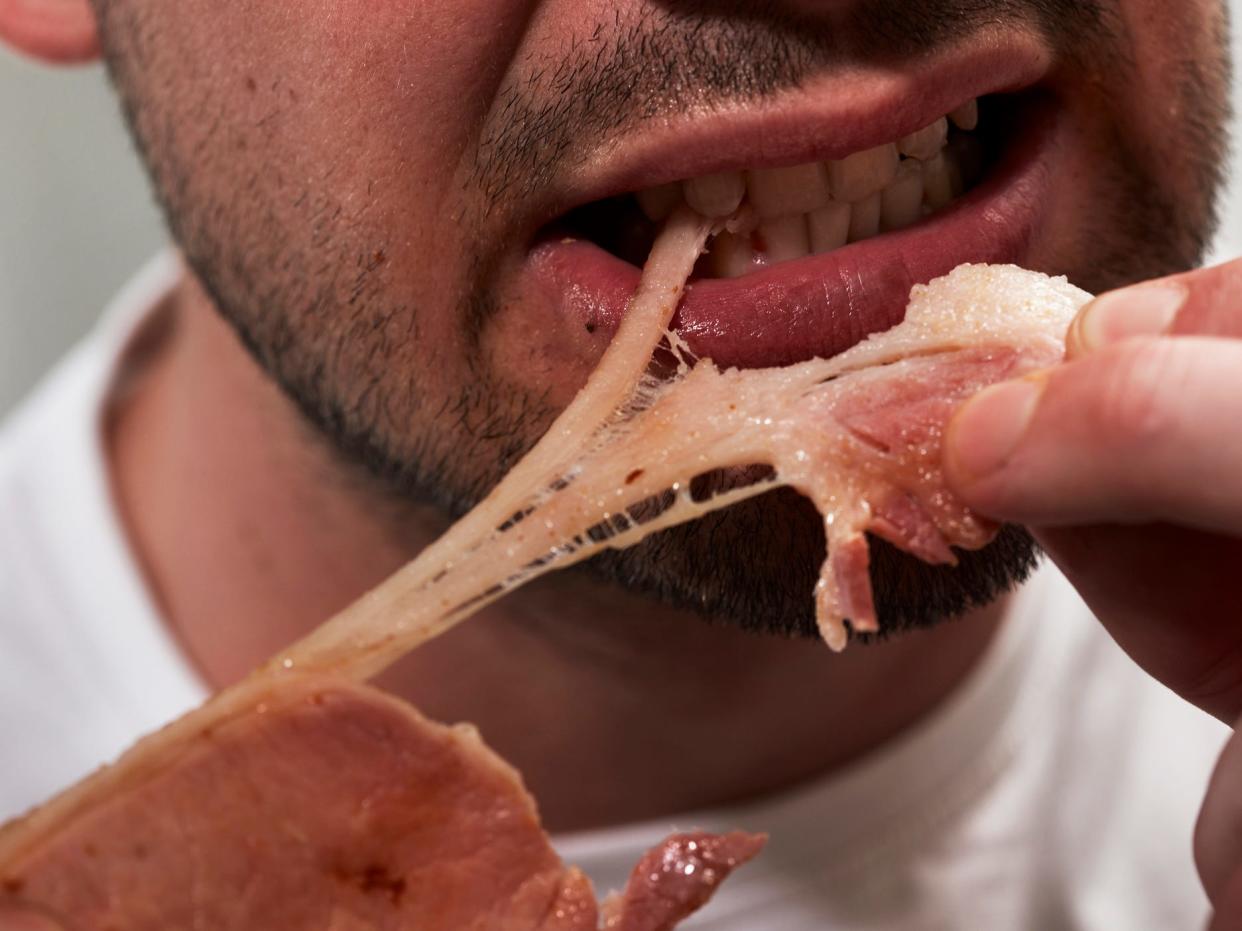 a close-up of a man with facial hair eating a piece of meat he's holding in his hands