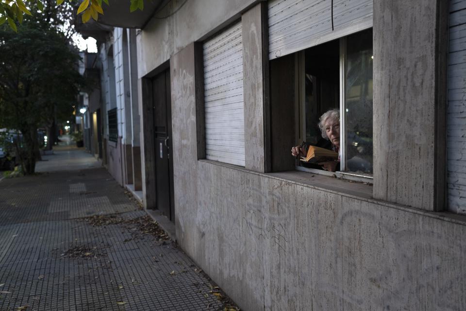 A woman takes a break from reading a book from a window at her home in Buenos Aires, Argentina, Monday, May 8, 2023. (AP Photo/Rodrigo Abd)