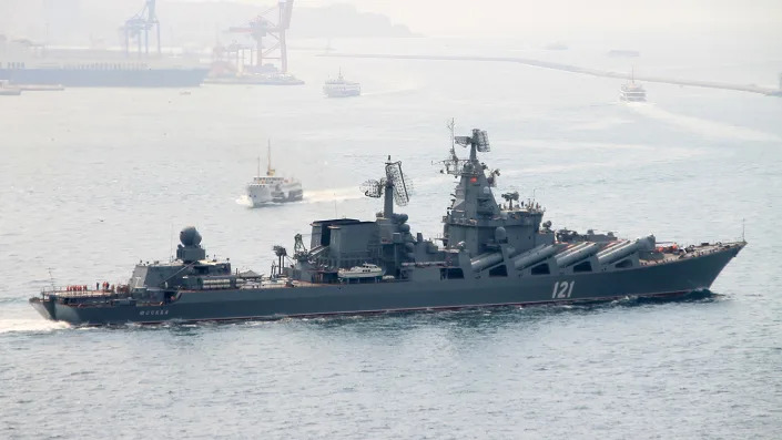 A warship in a harbor near other boats.