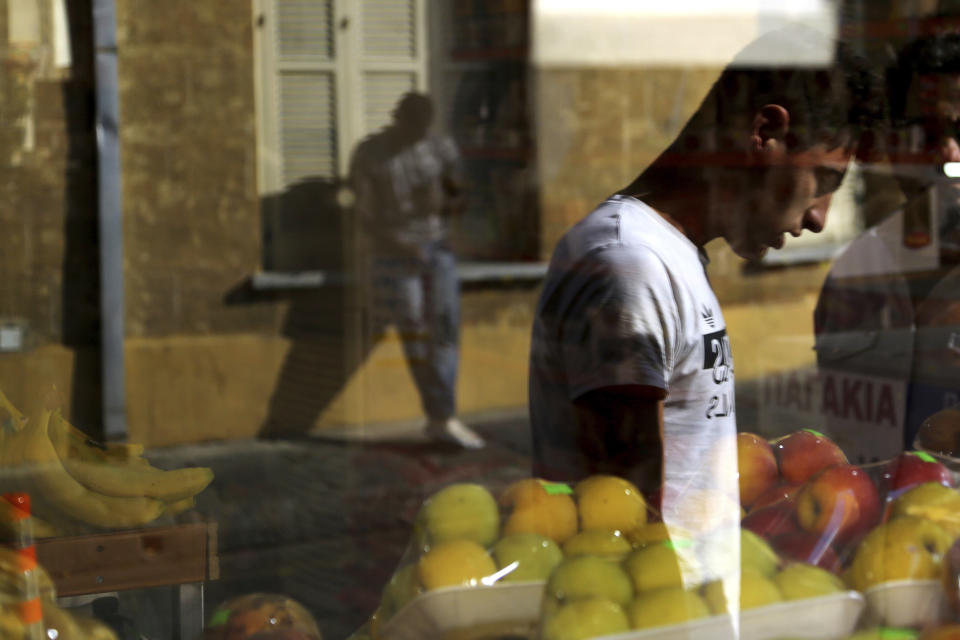 In this Tuesday, Nov. 20, 2018, migrants reflected on a window of a market at a neighborhood in central city of Nicosia, Cyprus. Migrant arrivals are down overall in Europe as some countries tighten their borders, but migrant trafficking networks seem to have set their sights on Cyprus. (AP Photo/Petros Karadjias)