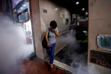 A woman covers her face from tear gas after a sit-in at Yoho mall at Yuen Long to protest against violence that happened two months ago when white-shirted men wielding pipes and clubs wounded both anti-government protesters and passers-by, in Hong Kong