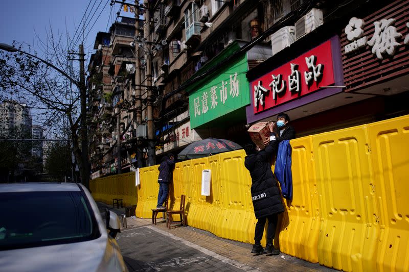 Residents pay for groceries over barriers set up to ring fence a wet market on a street in Wuhan