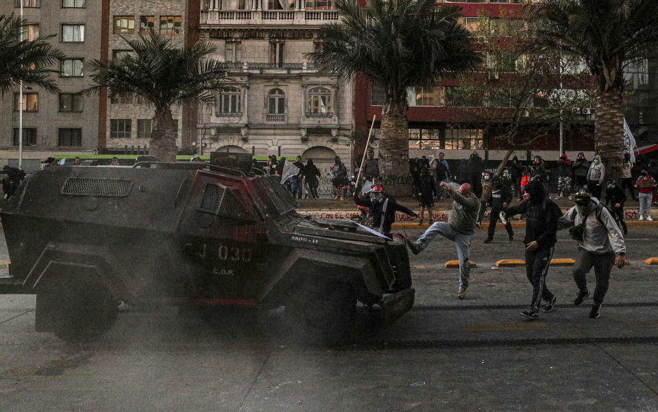 A demonstrator kicks a police armored vehicle during a protest against police in reaction to a video that appears to show an officer pushing a youth off a bridge the previous day at a protest, in Santiago, Chile, Saturday, Oct. 3, 2020. (AP Photo/Esteban Felix)
