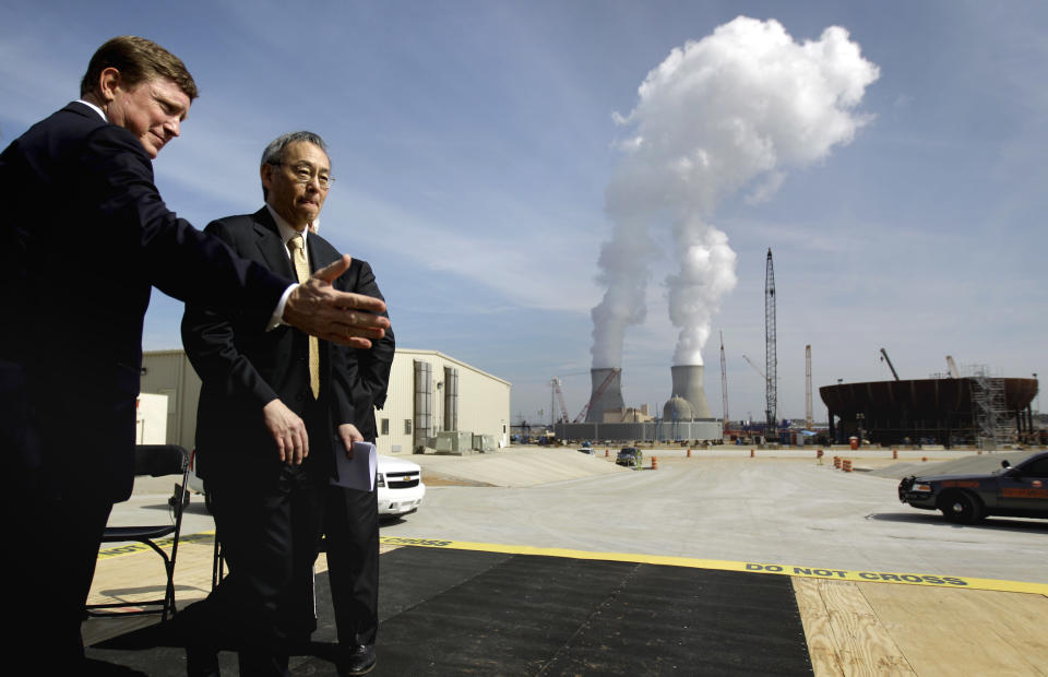 FILE- In this Feb. 15, 2012 file photo, U.S. Secretary of Energy Secretary Steven Chu, right, exits the stage with Southern Company President and CEO Thomas Fanning as cooling towers for units 1 and 2 are seen in the background at left as the new reactor vessel bottom head for unit 3 stands under construction at right, on a visit of the Vogtle nuclear power plant in Waynesboro, Ga. Vogtle initially estimated to cost $14 billion, has run into over $800 million in extra charges related to licensing delays. A state monitor has said bluntly that co-owner, Southern Co. can’t stick to its budget. The plant, whose first reactor was supposed to be operational by April 2016, is now delayed seven months. (AP Photo/David Goldman, File)