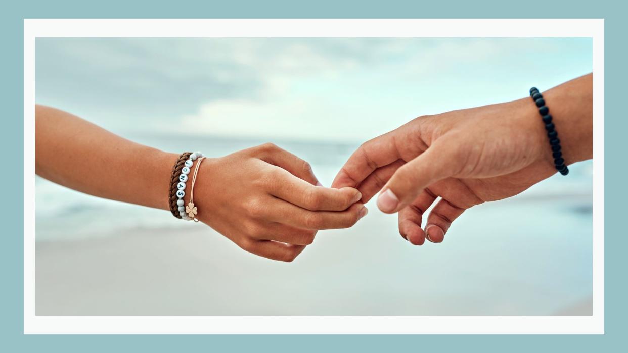  How often does your partner think about breaking up? Pictured: Couple's hands splitting apart with the beach in the background 