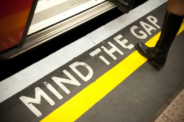 The leg and boot of a woman stepping into a tube carriage, and crossing the yellow line of the world famous 'Mind the gap' signa
