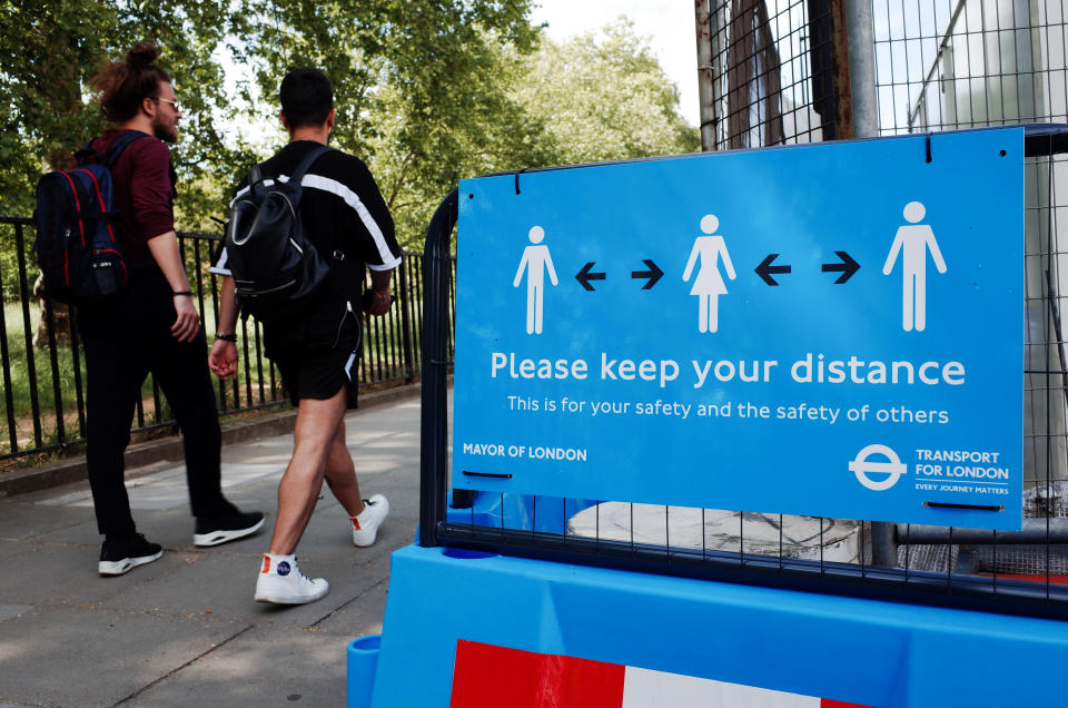 Two men walk past a sign reminding people to observe social distancing on Park Lane in London, England, on May 18, 2020. Britain began its ninth week of coronavirus lockdown today, a day after the lowest reported covid-19 death toll (170) across the country since March. A day of even lower covid-19 fatalities today (160) is meanwhile cementing hopes that the UK is firmly into the recovery phase of its coronavirus crisis, and that its continued emergence from lockdown will be able to carry on as planned. (Photo by David Cliff/NurPhoto via Getty Images)