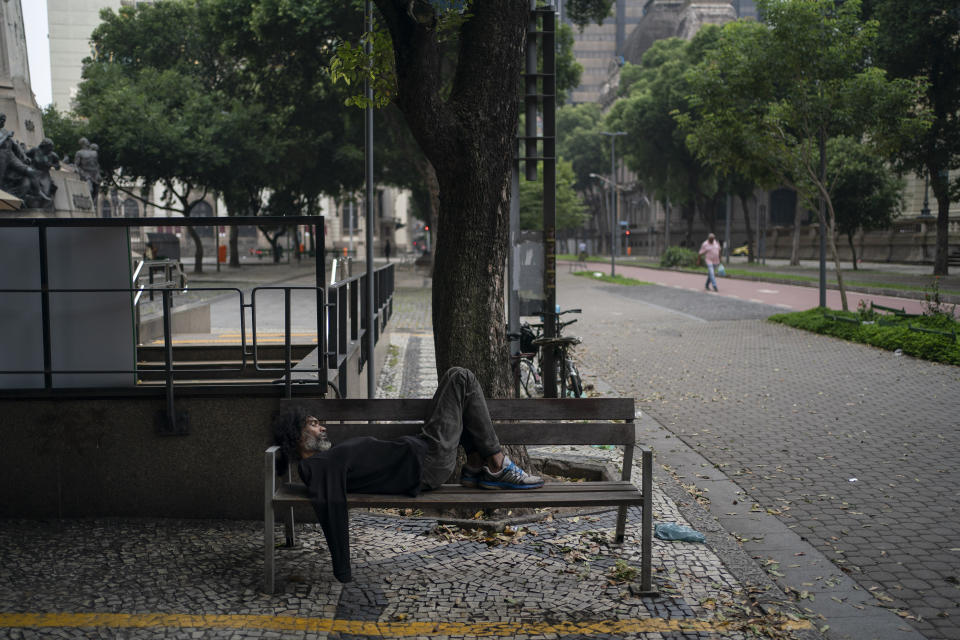 A homeless man sleeps on a bench in an empty downtown Rio de Janeiro, Brazil, Monday, March 30, 2020, while most other residents stay inside indoors to help contain the spread of the new coronavirus. (AP Photo/Leo Correa)