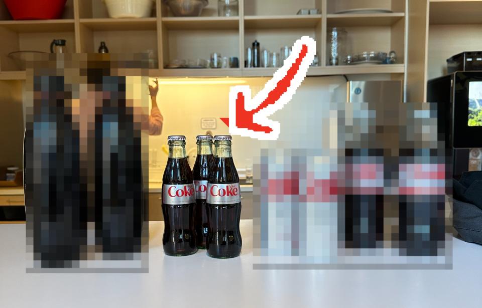 The four different types of Diet Coke lined up on a table, with an arrow pointing to the glass bottle