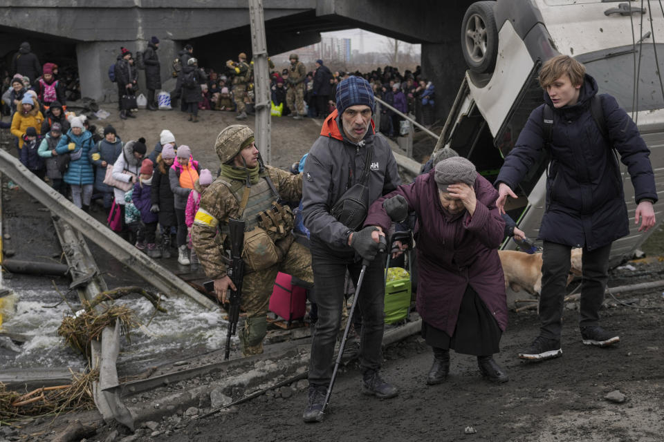 An elderly lady gets assisted while crossing the Irpin river, under a bridge that was destroyed, as civilians flee the town of Irpin, Ukraine, Saturday, March 5, 2022. (AP Photo/Vadim Ghirda)