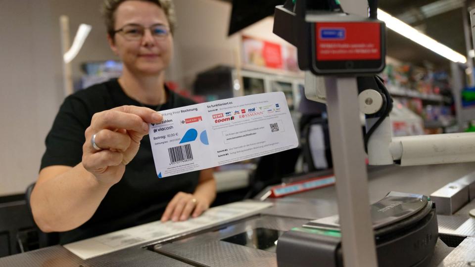 Eine Mitarbeiterin in einer Filiale des Einzelhändlers REWE hält ein Blatt mit einem Barcode in der Hand. Mit diesem Abschnitt sollen Bürger in Köln ihre Knöllchen künftig einfach an Supermarktkassen begleichen können.