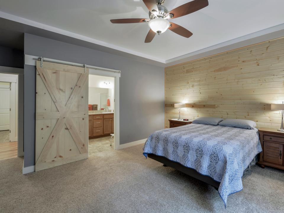 A bedroom with barn door on the left, and a fan on ceiling and bed on the right