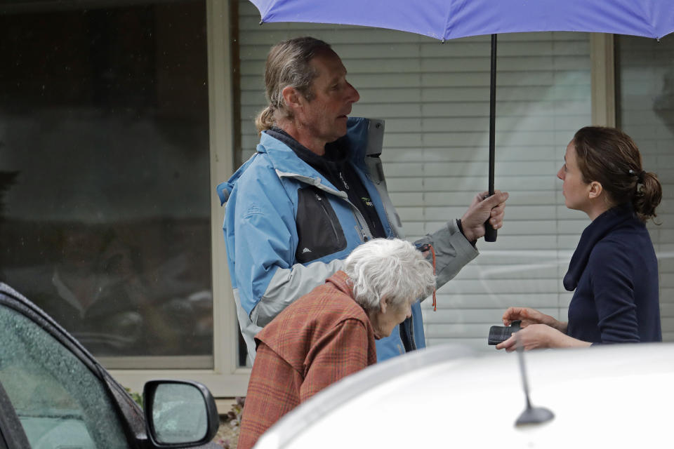 In this March 6, 2020 photo, Charlie Campbell, center stands with his mother, Dorothy Campbell, as they talk with a worker about his father, Gene Campbell, who can be seen through a window at left, at the Life Care Center in Kirkland, Wash. Charlie is nearly 13 years sober, but said he has been feeling tested due to stress from having his father now recovering from the new coronavirus in a hospital, and several other sources of worry and stress in his life. (AP Photo/Ted S. Warren)