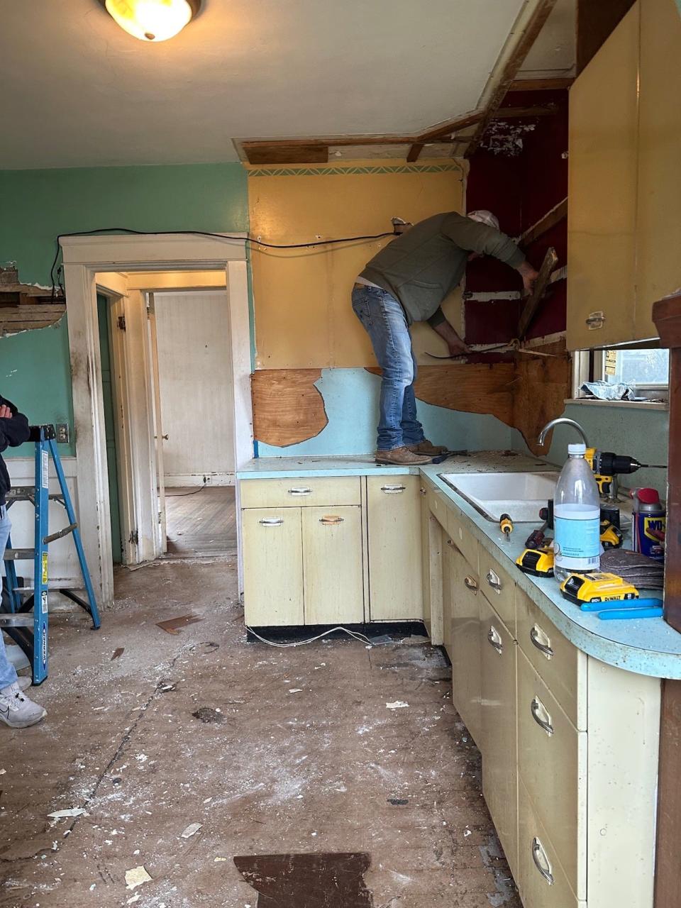 A man stands on top of a kitchen counter as he's renovating the space.