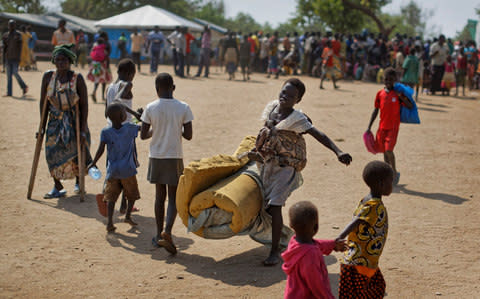 A South Sudanese refugee girl with a baby on her back carries a foam mattress to the communal tent where they will sleep - Credit:  Ben Curtis/AP