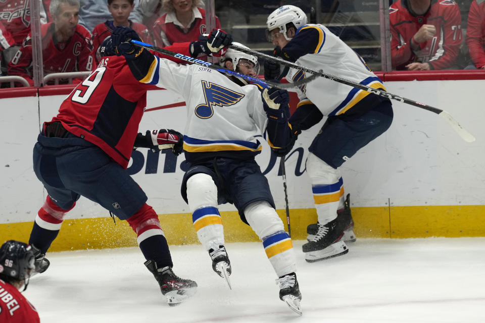 CORRECTS DAY TO FRIDAY - Washington Capitals center Aliaksei Protas (59) collides with St. Louis Blues defenseman Nick Leddy, center, as Blues center Robert Thomas (18) works for the puck during the first period of an NHL hockey game Friday, March 17, 2023, in Washington. Protas was called for a holding penalty. (AP Photo/Carolyn Kaster)