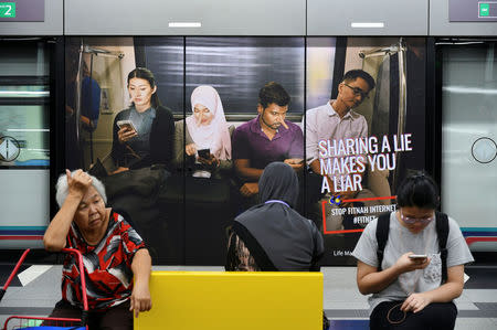 Commuters sit in front of an advertisement discouraging the dissemination of fake news, at a train station in Kuala Lumpur, Malaysia March 28, 2018. REUTERS/Stringer/Files