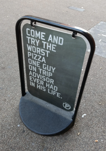 Sidewalk sign inviting people to try "the worst pizza one guy on TripAdvisor ever had."