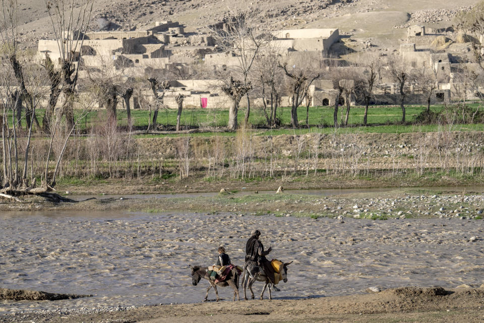 A man and his child cross a river with their donkeys to bring home pots of drinking water from a spring in a remote region of Afghanistan, on Thursday, Feb. 23, 2023. In a nearby village, a baby was orphaned during a U.S. raid in 2019. A Marine who adopted her claims her parents were foreign fighters. But villagers say they were innocent farmers caught in the fray. (AP Photo/Ebrahim Noroozi)