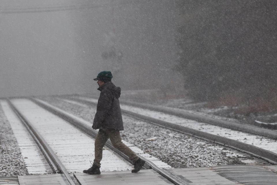 A man walks across the railroad tracks as snow falls in downtown Ramsey, NJ on Tuesday March 14, 2023. 