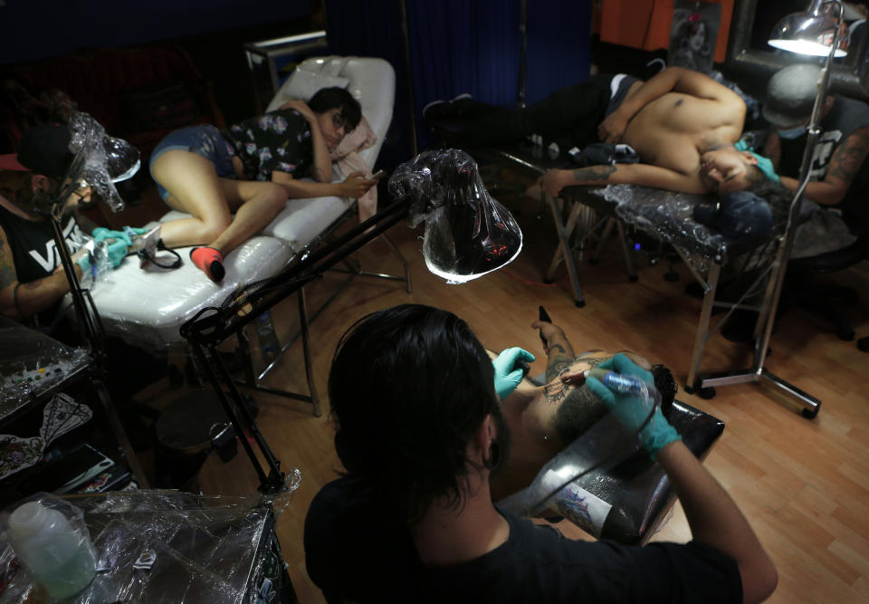 En esta foto del 18 de abril de 2019, los tatuadores Lalo Aguayo, a la izquierda, Lalo Calva, centro, y Emanuel Arana, trabajan con los clientes Laura Reyes, Adrián Alonso Rodríguez y Jonathan Brannan en el salón de tatuajes Corona en la Ciudad de México. (AP Foto / Marco Ugarte)