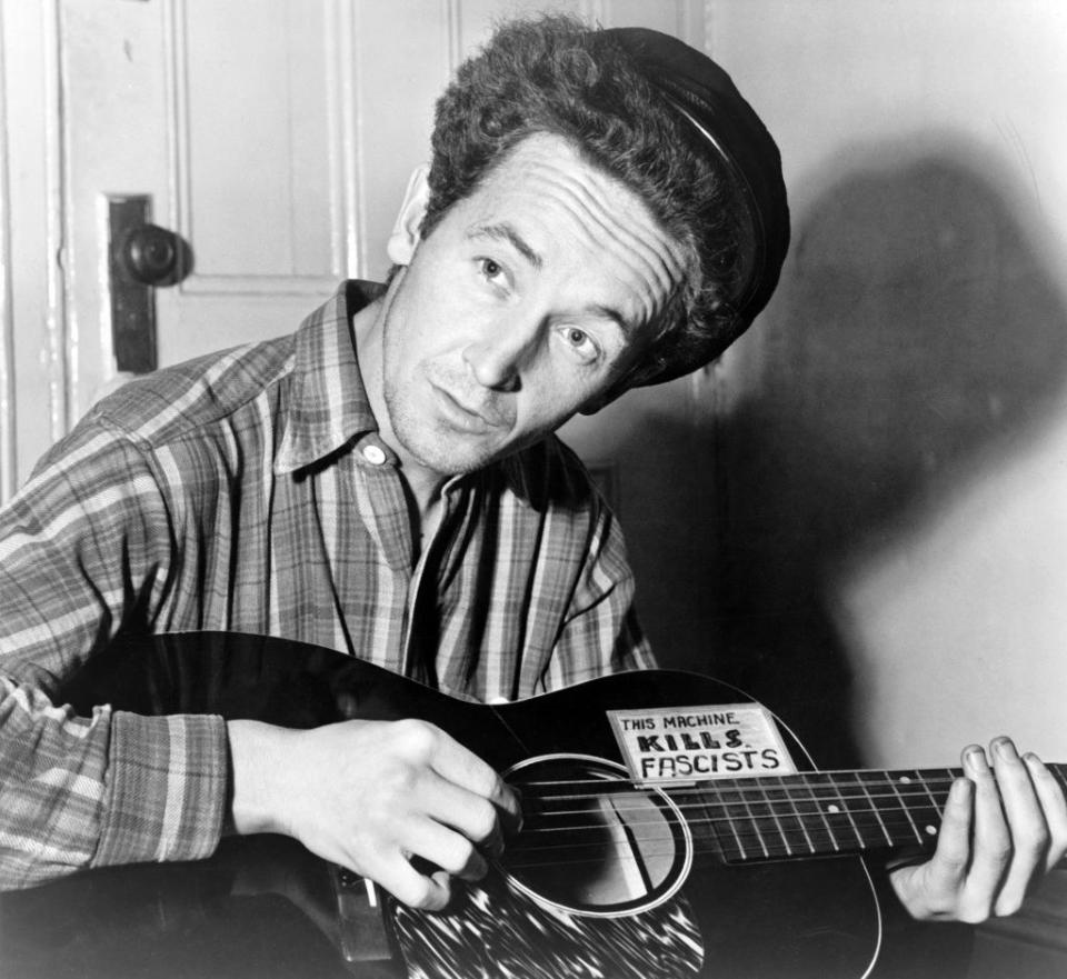 Woody Guthrie holding his "this machine kills fascists" guitar