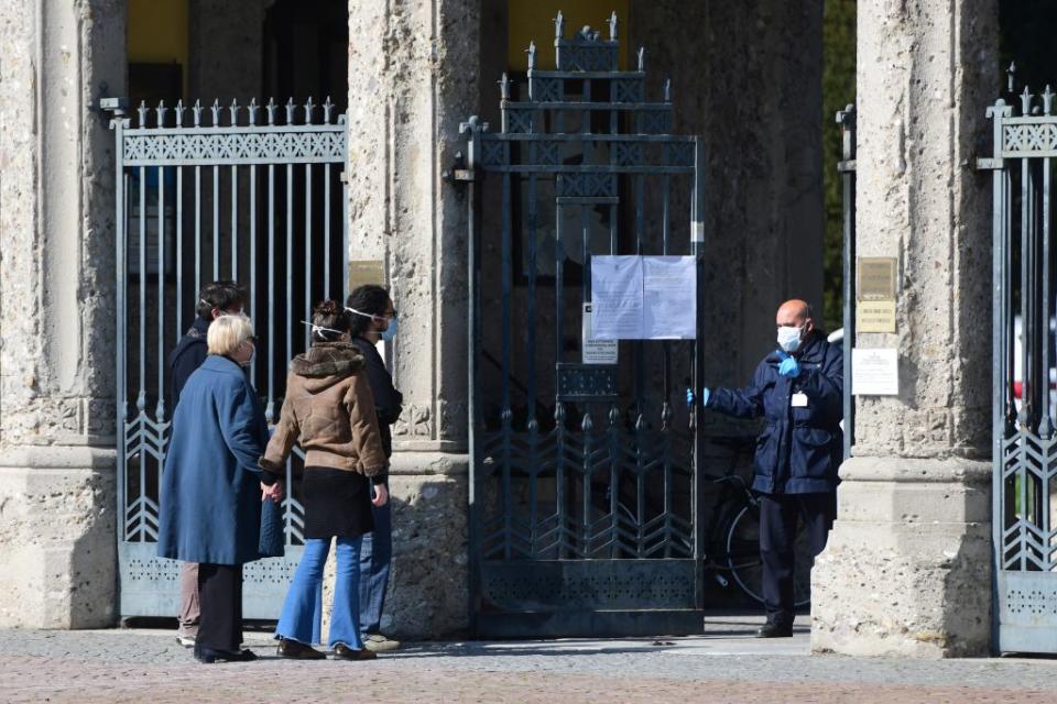 A cemetery employee wearing a face mask closes the gates of the Monumental cemetery of Bergamo on relatives of a person who died from coronavirus. Source: Getty