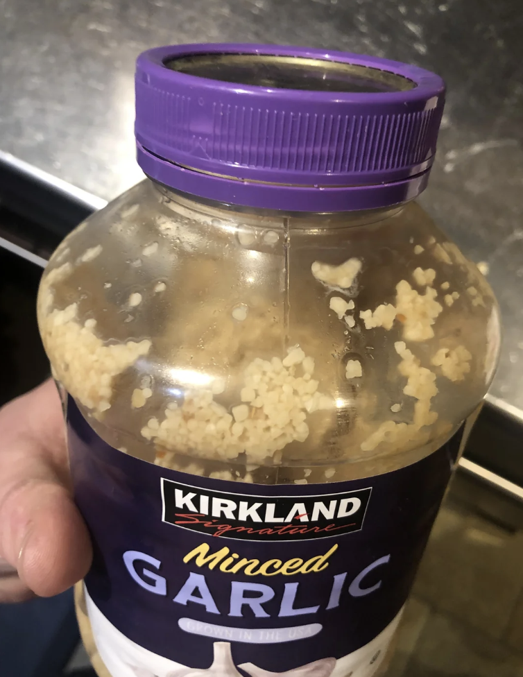 Person holding a Kirkland minced garlic jar with garlic pieces stuck to the lid