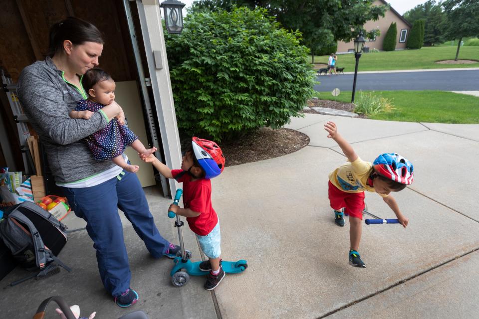 After picking up her kids at day care, Sarah Jasti waits for her husband to come from work at their home in Menomonee Falls. Sarah holds 3-month-old daughter Nina while 3-year-old son Ari holds Nina's foot and Jude, 5, dismounts a scooter. Her husband, Jamie Jasti, is a second-year emergency medical resident at Froedtert Hospital.