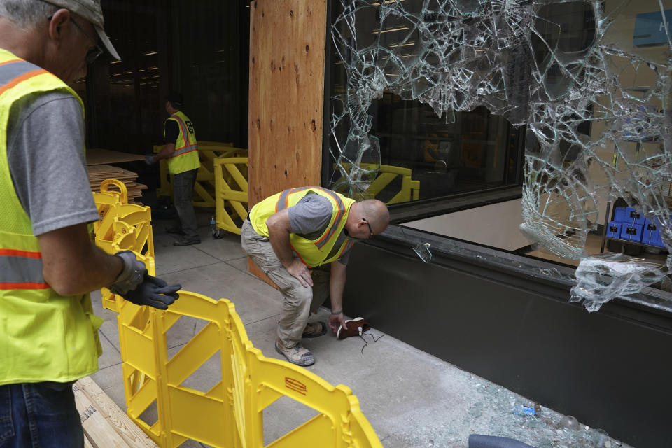 A worker picks up a shoe outside one of the broken windows at the Nordstrom Rack on Nicollet Mall, Thursday, Aug. 27, 2020, in Minneapolis, where several businesses were damaged by a group of looters Wednesday night after the suicide of a homicide suspect on the Mall ignited rioting. (Anthony Souffle/Star Tribune via AP)