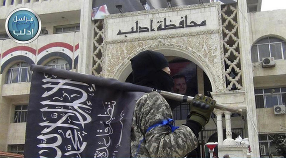 FILE - In this file photo posted on the Twitter page of Syria's al-Qaida-linked Nusra Front on March 28, 2015, a fighter from Syria's al-Qaida-linked Nusra Front holds his group flag as he stands in front of the governor building in Idlib province, north Syria. Turkey and Russia appear to have succeeded in creating a demilitarized zone along the frontlines of Syria's flashpoint Idlib region, after rebels and an al-Qaida-linked alliance pulled back their heavy weaponry in accordance with the agreement. (Al-Nusra Front Twitter page via AP, File)