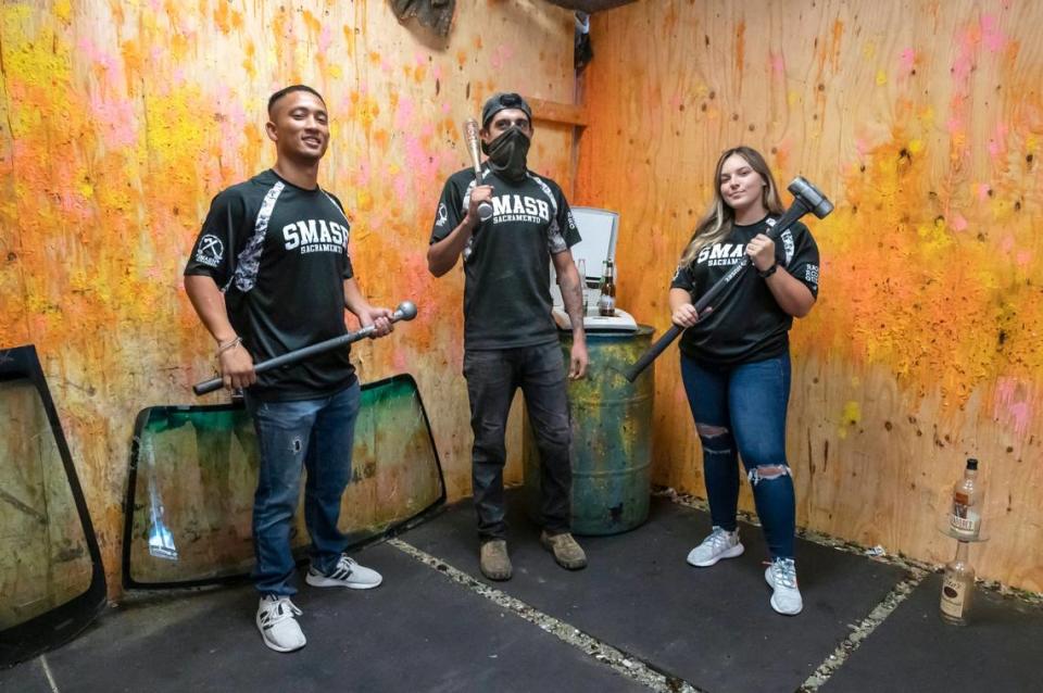 Owner David Messier, left, “rage room” guide Lip Villarreal, center, and manager Breanna Wilkie pose Monday with “weapons” used to destroy things at Smash Sacramento in Carmichael. Messier, an Army veteran, opened the location in 2018 and has since added a second location in downtown Sacramento.