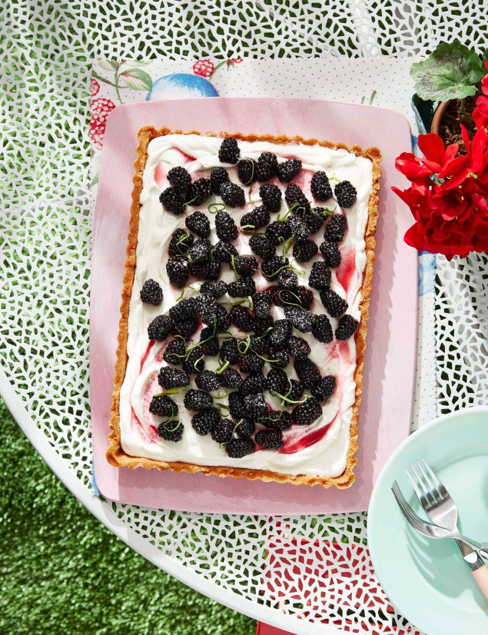 blackberry coconut tart topped with fresh blackberries and lime zest on a tray on an outdoor table
