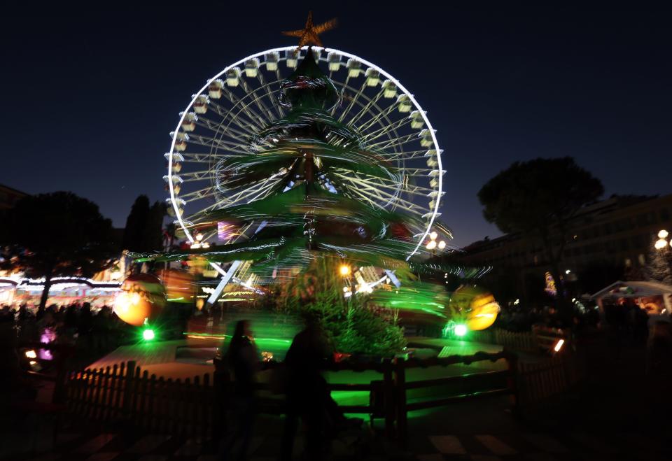 People walk past a giant Christmas tree near a Ferris wheel on the place Massena as part of Christmas holiday season illuminations in Nice