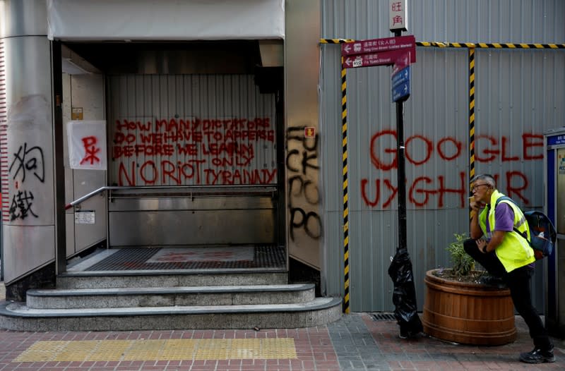 A man smokes a cigarette in front of a closed entrance of subway station which was vandalized during an anti-government rally in Hong Kong