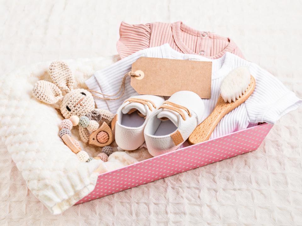 A gift basket for a baby with shoes, toys, a brush, clothes, and a blanket.