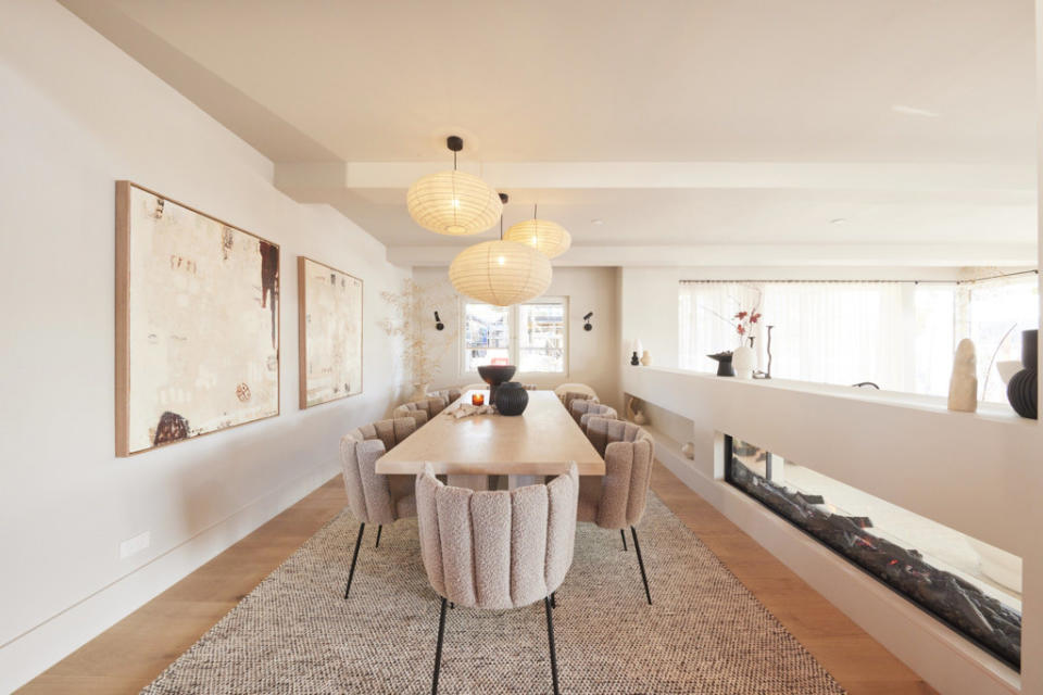 A wide shot from the head of a dining table, pictures on the left hand wall and hanging material light covers. 