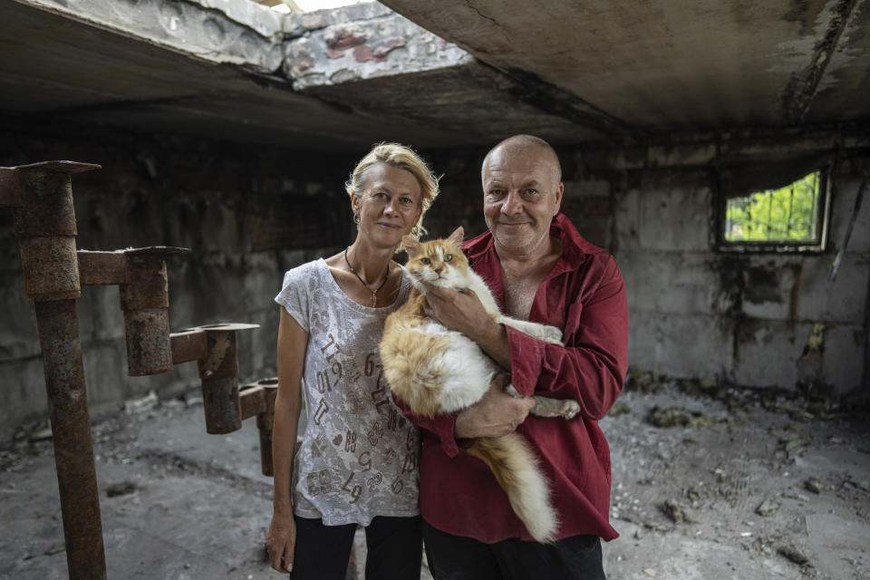 Zhanna Dynaeva and Serhiy Dynaev stand with a cat inside their house which was destroyed by Russian bombardment, in the village of Novoselivka, near Chernihiv, Ukraine, Saturday, Aug. 13, 2022. Residents in many heavily-damaged areas in Ukraine have set up their own initiatives to rebuild homes before the winter as international organizations rush aid to Ukraine to help with the reconstruction effort. (AP Photo/Evgeniy Maloletka)