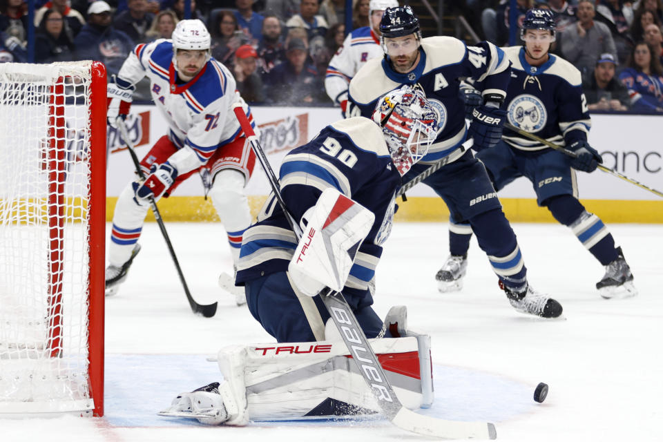 Columbus Blue Jackets goalie Elvis Merzlikins (90) makes a stop in front of New York Rangers forward Filip Chytil (72) and Blue Jackets defenseman Erik Gudbranson (44) during the first period of an NHL hockey game in Columbus, Ohio, Saturday, Oct. 14, 2023. (AP Photo/Paul Vernon)