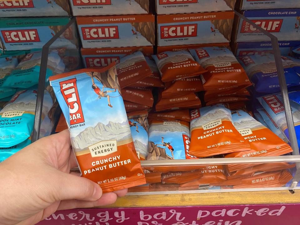 hand holding a clif bar in front of a shelf of clif bars at trader joes