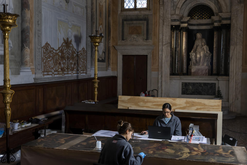 Restorers Annalisa Tosatto, right, and Alice Chiodelli work at the conservation and study of ' The reward and a pair of putti', a 1590 painting by Venetian Renaissance artist Andrea Michieli known as Andrea Vicentino in a makeshift laboratory set up in the Venetian Doge's private chapel inside Palazzo Ducale in Venice, northern Italy, Wednesday, Dec. 7, 2022. The 93x330 centimeters (approximately 36.6x130 inches) canvas was adorning the Grimani's Hall in the Doge's apartments of Palazzo Ducale. In the background Jacopo Sansovino's marble statue 'Madonna with child and angels'(1536-37). (AP Photo/Domenico Stinellis)