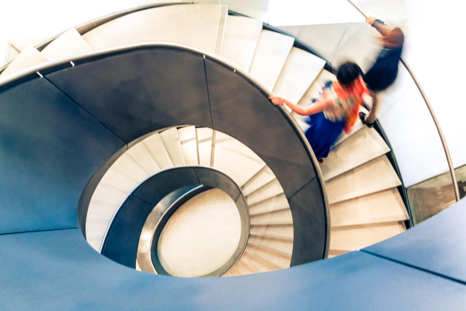 Overhead view depicting blurred motion of people walking up and down a spiral staircase. The people are completely blurred, and the slow shutter speed makes it appear as though the people are moving fast. Image taken at City Hall in London, which is a publicly owned building that is accessible to the general public without any photographic restrictions. Room for copy space.