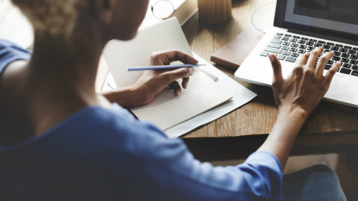 Lady making handwritten notes next to a computer