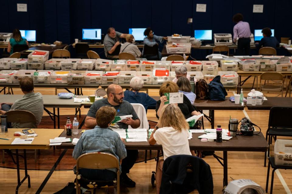 People sitting at tables with containers full of ballots